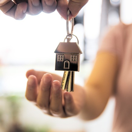 A photo of two hands, one of them holding keys with a keychain illustrating a house.